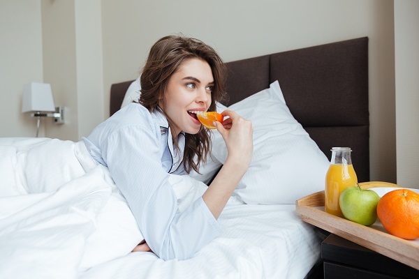 Happy young smiling Ukrainian lady under a blanket eating an orange and drinking juice